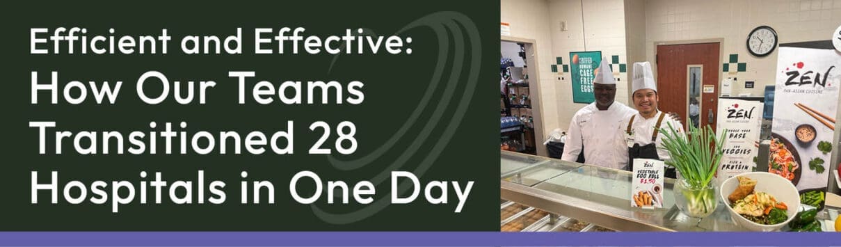 Two chefs stand behind a prepared meal counter with vegetable displays and signs about healthy eating.